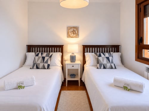 Dormitorio doble en el apartamento A Dourada de Holibai Baiona con ropa de cama blanca, almohadas geométricas, camas de madera y vistas al mar