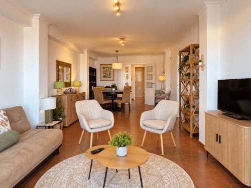 Sala de estar luminosa y moderna en el apartamento A Dourada de Holibai en Baiona, con sillones color crema, muebles de madera y vistas al mar