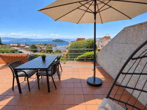 Terraza con vistas al mar de Baiona en Holibai con mesa de comedor, sombrilla y paisaje costero