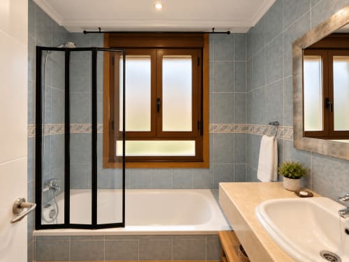 Baño moderno en apartamento A Dourada de Holibai, Baiona con azulejos grises, bañera blanca, cabina de ducha negra y tocador de madera
