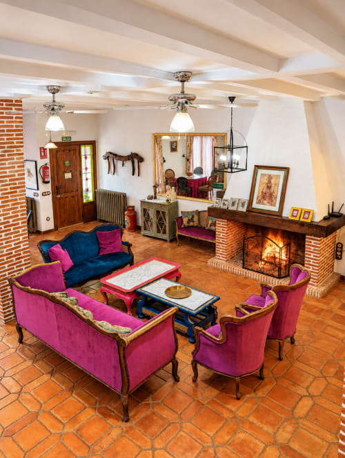 Acogedora sala de estar colorida con sillones de terciopelo rosa, chimenea, vigas de madera y pisos de barro en El Descanso del
