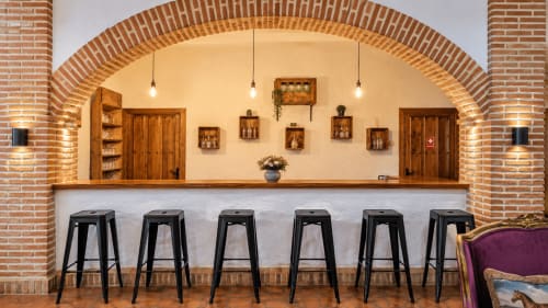 Mostrador de bar moderno con taburetes negros bajo arco de ladrillo rústico en la villa boutique El Descanso del Peregrino en Guadalupe,