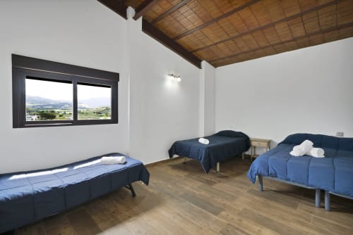 Habitación espaciosa de la casa rural Holiday Dreams Ronda con tres camas, vigas de madera y vistas panorámicas del valle