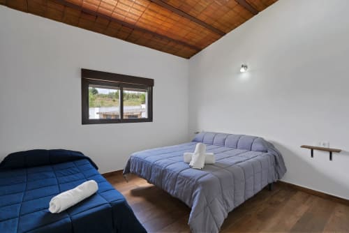 Dormitorio luminoso de la casa Holiday Dreams Ronda con dos camas azules, techo de madera, ventana con vistas a la Laguna Espejo