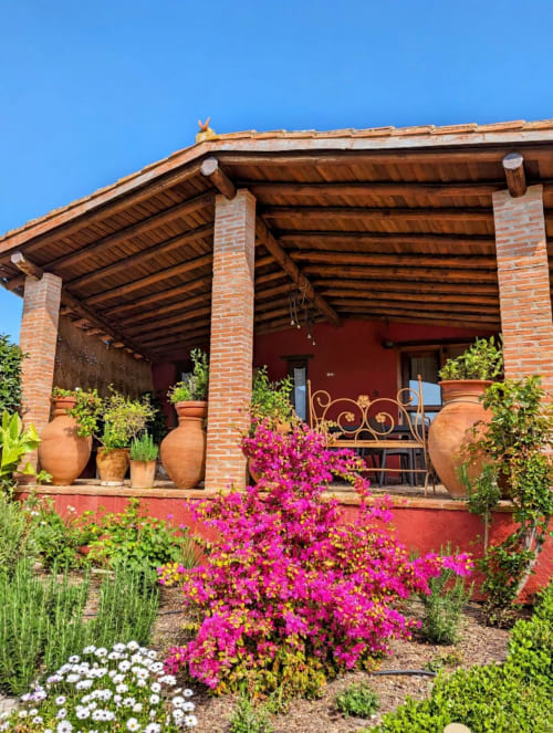 Casa de campo rústica con terraza roja, vigas de madera y buganvillas magenta en Guadalupe, Cáceres