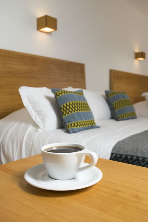 Taza de café sobre mesa de madera en el hotel Casa Cafeólogo de San Cristóbal de las Casas, México, con cama de fondo
