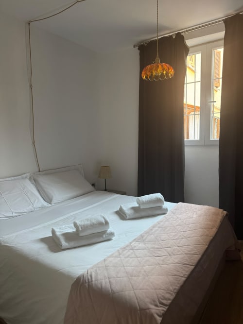 Modern bedroom at THE V Collection in Sormano with queen bed, white linens, golden pendant lamp, and mountain views through