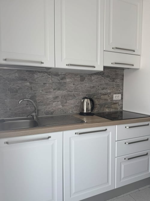 Modern kitchen in Sormano apartment with white cabinets, gray stone backsplash, and stainless steel appliances