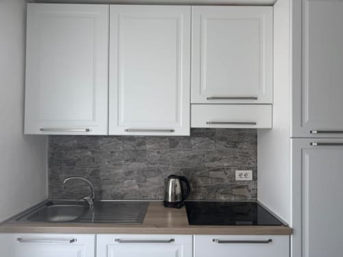 Modern kitchenette with white cabinetry, dark gray tile backsplash, and stainless steel appliances in Appartamento Sormano 2