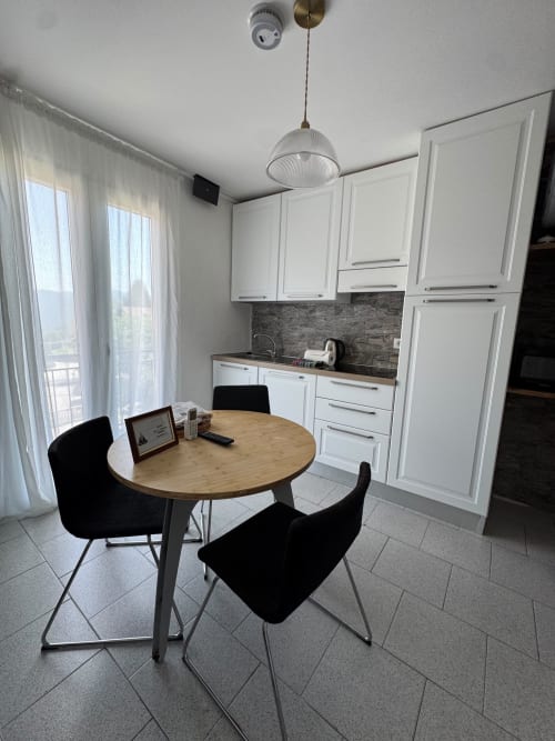 Modern kitchen-dining area in Appartamento Sormano 2 with white cabinetry, round wooden table, black chairs, and mountain