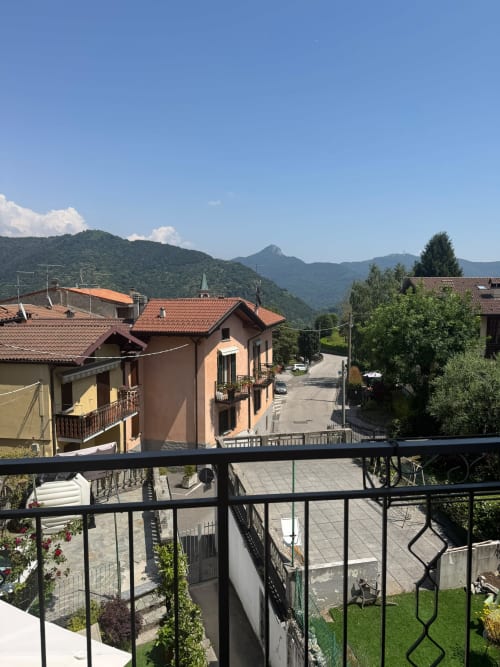 Balcony view of Sormano mountain village with terracotta-roofed apartments and green hills, THE V Collection