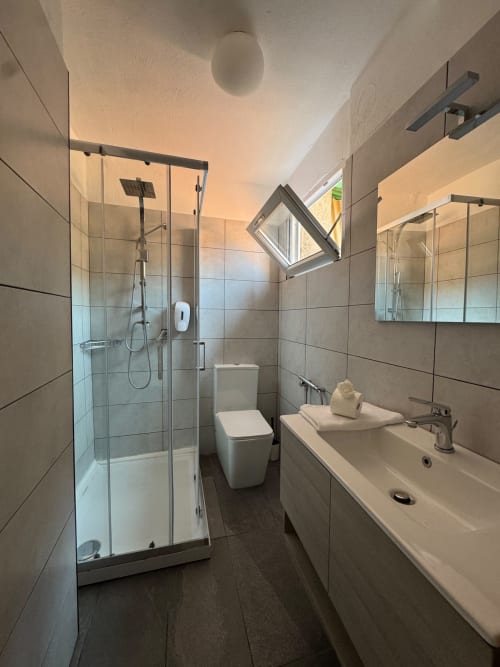 Modern bathroom in Appartamento Sormano 2 with walk-in shower, double sink, toilet, and skylight window at THE V Collection,
