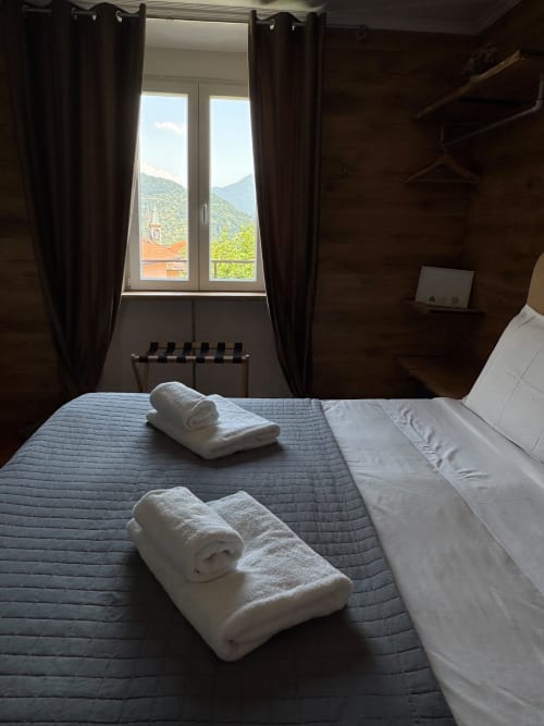 Camera con vista montagna in THE V Collection a Sormano con asciugamani bianchi arrotolati sul letto e tende scure