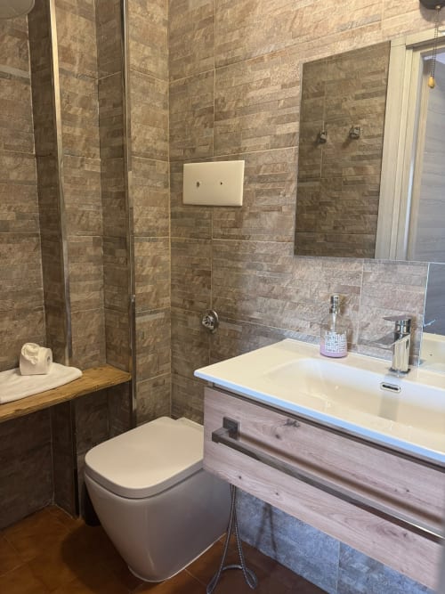 Bagno moderno nella collezione THE V Sormano con rivestimenti in piastrelle, lavabo bianco, toilette e box doccia