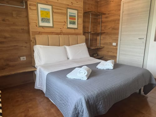 Spaziosa camera da letto nell'appartamento di Sormano con interni in legno, letto queen, cuscini bianchi e asciugamani arrotolati su biancheria grigia