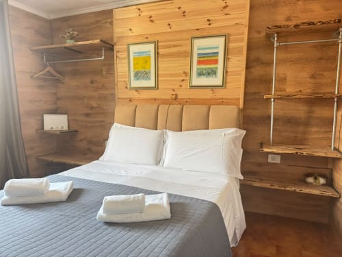 Camera da letto in stile rustico con letto matrimoniale, cuscini bianchi e asciugamani arrotolati presso THE V Collection a Sormano, Italia