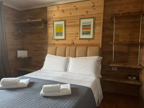 Camera spaziosa di THE V Collection Sormano con pareti in legno, letto matrimoniale, cuscini bianchi, asciugamani arrotolati, paesaggio incorniciato