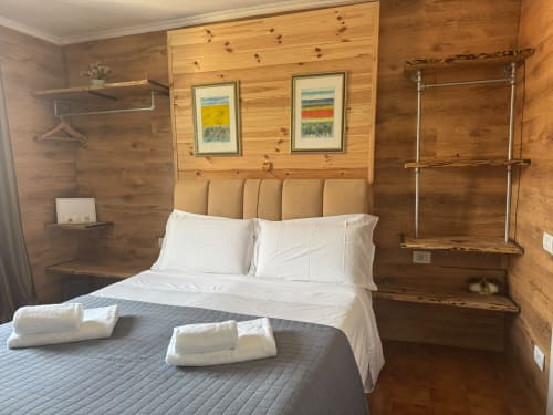 Camera da letto rustica in legno presso THE V Collection Sormano con letto matrimoniale, biancheria bianca e quadri con vista montagna