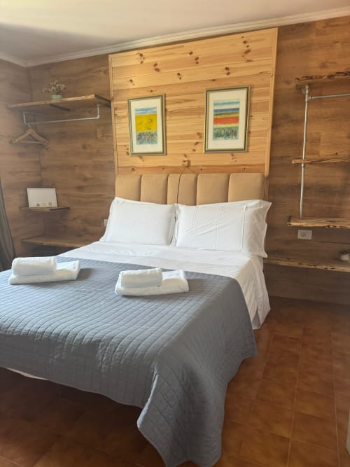 Camera da letto in stile rustico con vista montagna presso THE V Collection Sormano, con biancheria bianca e opere d'arte paesaggistica incorniciate