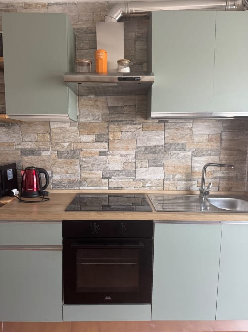 Cucina moderna nell'appartamento di Sormano con mobili salvia, rivestimento in pietra e elettrodomestici in acciaio inossidabile