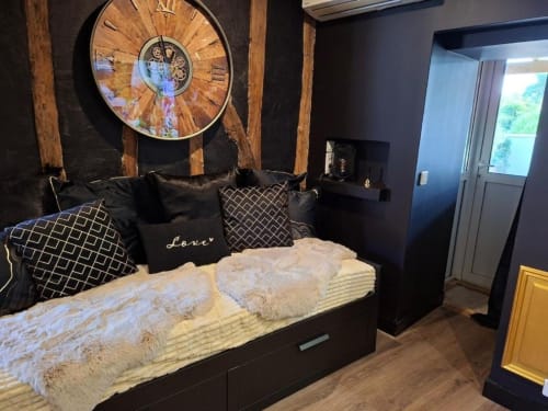 Chambre luxueuse avec lit noir, horloge murale décorative, détails dorés et équipements modernes à l'hôtel Love Room Sensation