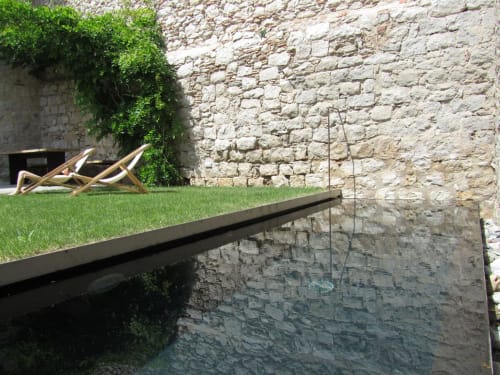 Alemanys 5 B&B courtyard with stone walls, reflecting pool, green lawn, and wooden loungers