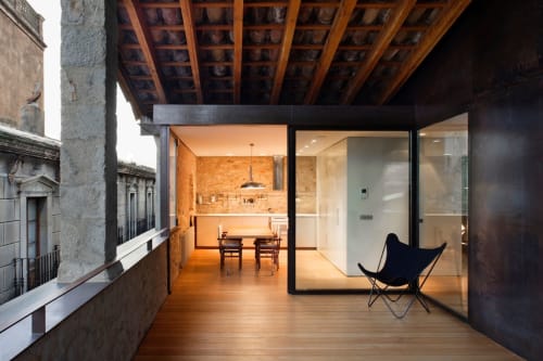 Modern terrace at Alemanys 5 Barcelona with wooden deck, glass-walled kitchen, and black butterfly chair overlooking historic
