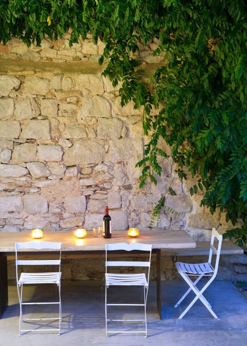 Outdoor dining terrace at Alemanys 5 with stone wall, ivy, wooden table, white chairs, and candlelight