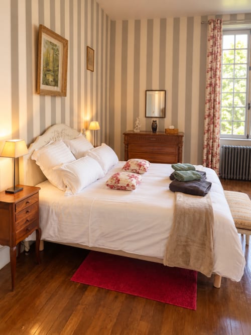 Élégante chambre double au Château de Montbrault avec papier peint rayé, mobilier en bois, literie blanche et vue sur le jardin