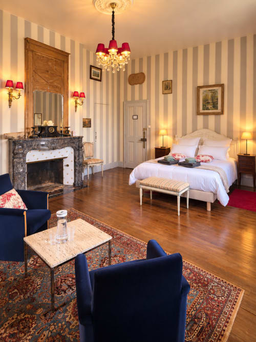 Chambre élégante du Château de Montbrault avec papier peint rayé, cheminée, lustre et mobilier luxueux