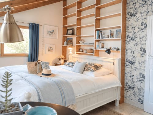 Helles Schlafzimmer in der Villa La Maison du Pêcheur mit Holzregalen, weißem Bett, blauen Akzenten und Blumentapete