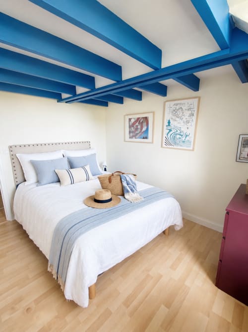 Helles Schlafzimmer mit blauen Deckenbalken, weißem Bett mit blauen Kissen und Bildern in der Villa Les Villas Du Bord De Mer