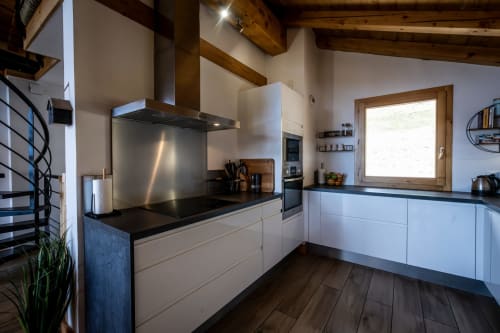 Cuisine contemporaine aux armoires blanches, plan de travail noir et poutres apparentes aux Chalets d'Aline, La Plagne