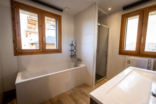 Salle de bain moderne aux Chalets d'Aline à La Plagne avec baignoire, douche, fenêtres en bois et revêtement chaleureux