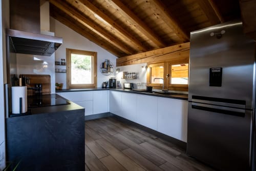 Cuisine moderne aux armoires blanches, comptoirs noirs, appareils en acier inoxydable et poutres en bois exposées aux Chalets