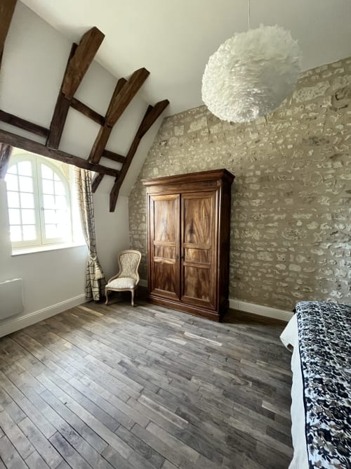 Chambre spacieuse du gîte 1694 avec poutres apparentes, murs en pierre, armoire en bois et parquet