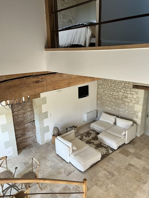 Gîte 1694 - séjour avec sièges crème, murs en pierre apparente et chambre en mezzanine à Scorbe Clairvaux