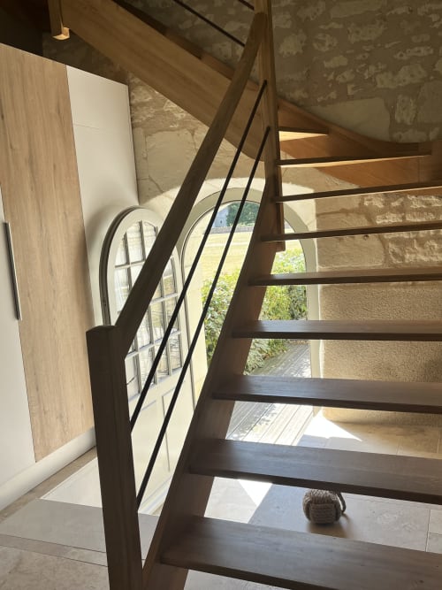 Escalier en bois moderne avec rampe métallique au Gite 1694, montrant le design intérieur et la lumière naturelle de la fenêtre