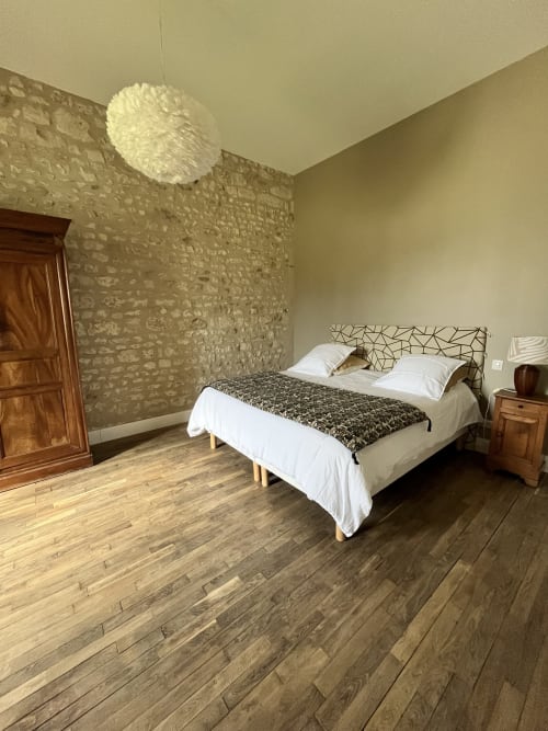 Chambre lumineuse au Gîte 1694 à Scorbe Clairvaux avec lit queen, mur en pierre, parquet et luminaire suspendu.