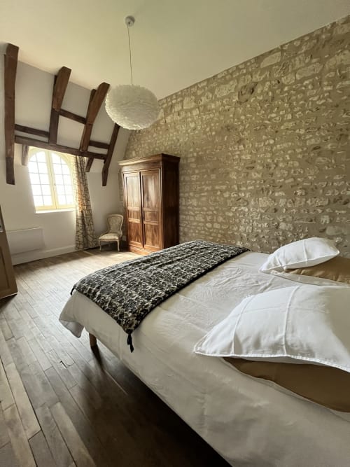 Chambre spacieuse au Gîte 1694 avec lits jumeaux, murs en pierre, poutres en bois et luminaires suspendus à Scorbe Clairvaux.