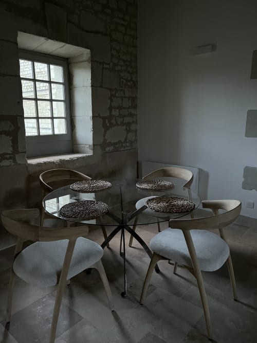 Salle à manger contemporaine du gîte 1694 avec table en verre, sets de table tressés et chaises en bois clair près de la fenêtre