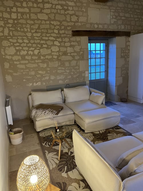 Salon cosy du gîte 1694 à Scorbe Clairvaux avec canapé crème, lampe tressée et murs en pierre
