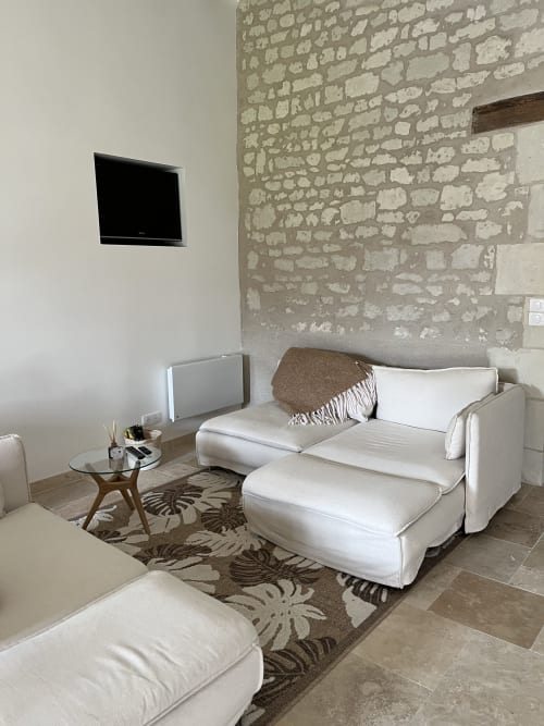 Coin lounge moderne du gîte 1694 avec canapé crème, mur en pierre apparente, table basse en bois et téléviseur mural
