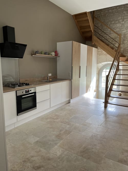 Cuisine moderne du gîte Petit Gîte 1694 avec armoires blanches, cuisinière à gaz, hotte noire et escalier en bois