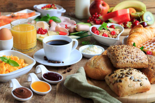 Desayuno completo en Hotel Rural Alto Gredos con café, frutas frescas, panes, cereales y pasteles sobre mesa de madera