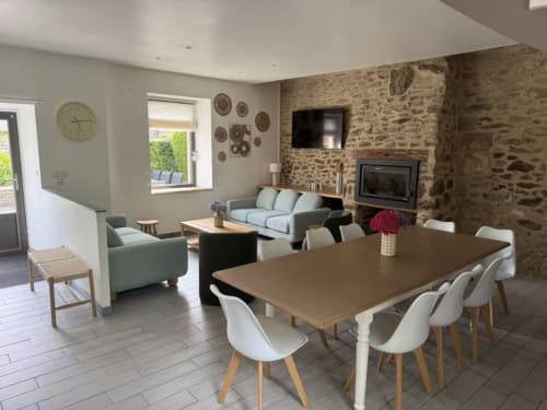 Salle à manger et séjour du Clos de l'Arguenon avec cheminée en pierre, table en bois et mobilier contemporain à Val-d'Arguenon