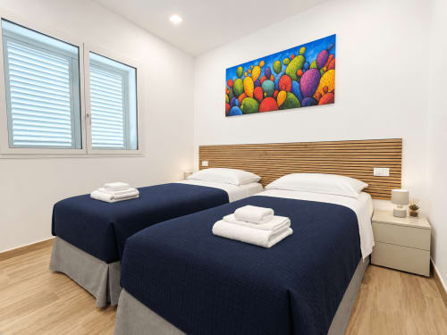 Modern twin bedroom at Villa Eraklea B&B in Noto with navy beds, wood headboard, colorful cactus art, and bright windows