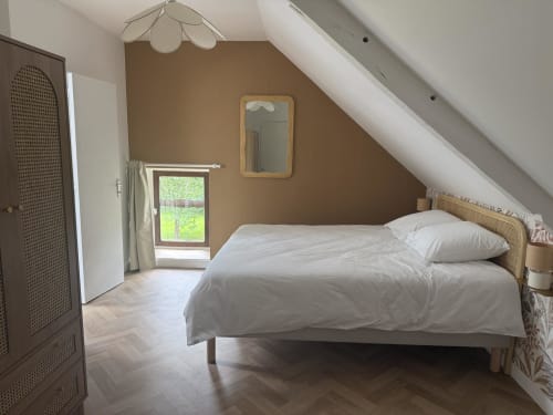 Chambre lumineuse au grenier du Clos de l'Arguenon avec murs beige, lit en bois et vue sur le jardin.