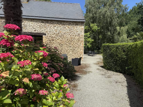 Charmante cour en pierre du Clos de l'Arguenon avec fleurs roses et haies taillées à Val-d'Arguenon