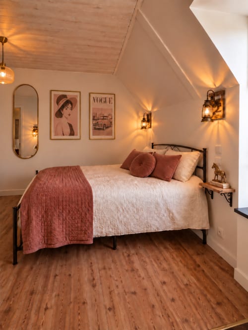 Chambre rétro-chic à L'Echappée Baie B&B avec lit en métal, éclairage chaleureux, affiche Vogue vintage et parquet